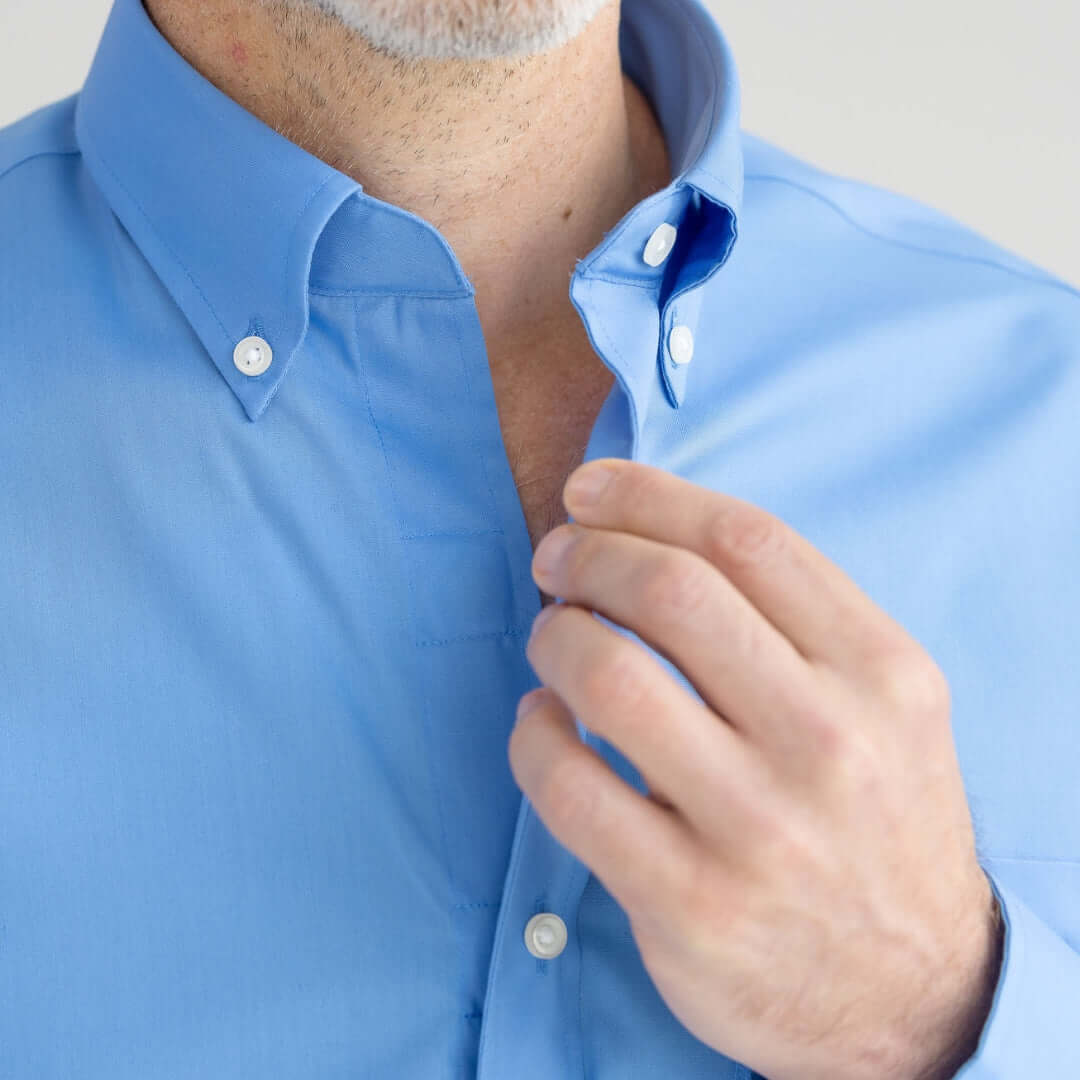 Stylish man adjusting the collar of a light blue button-up shirt.