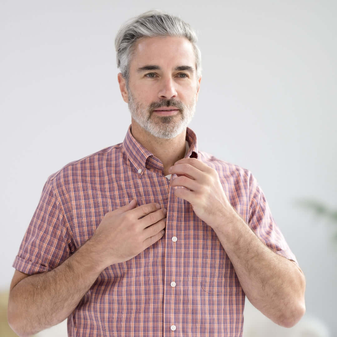 Man adjusting his Orange Plaid Short Sleeve Button Down Collar Shirt with Magnetic Closures, designed for adaptive wear.