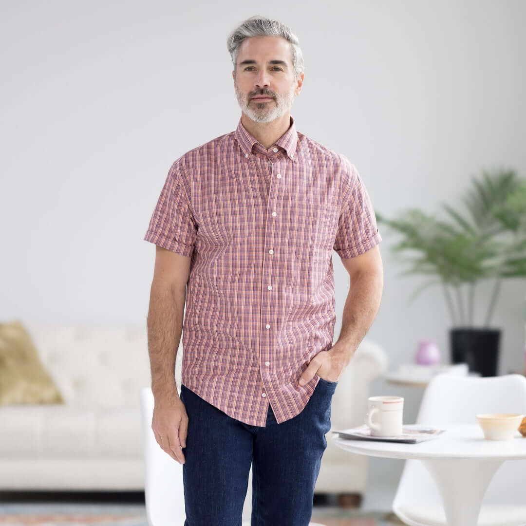 Man wearing orange plaid short sleeve button-down shirt with magnetic closures, in modern living room setting.