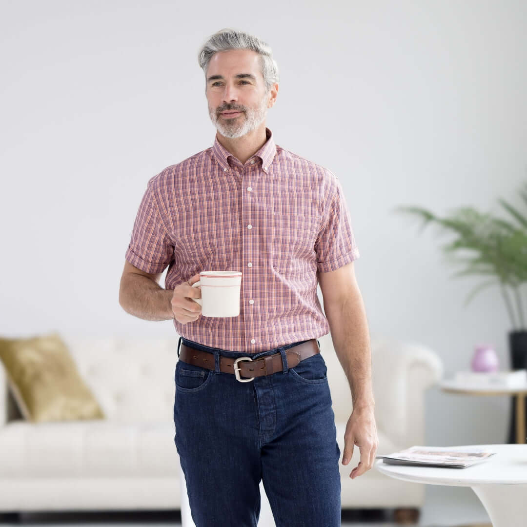 Man wearing an orange plaid short sleeve button-down collar shirt, holding a cup in a bright indoor setting.