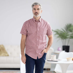 Man wearing orange plaid short sleeve button-down shirt with magnetic closures, in modern living room setting.