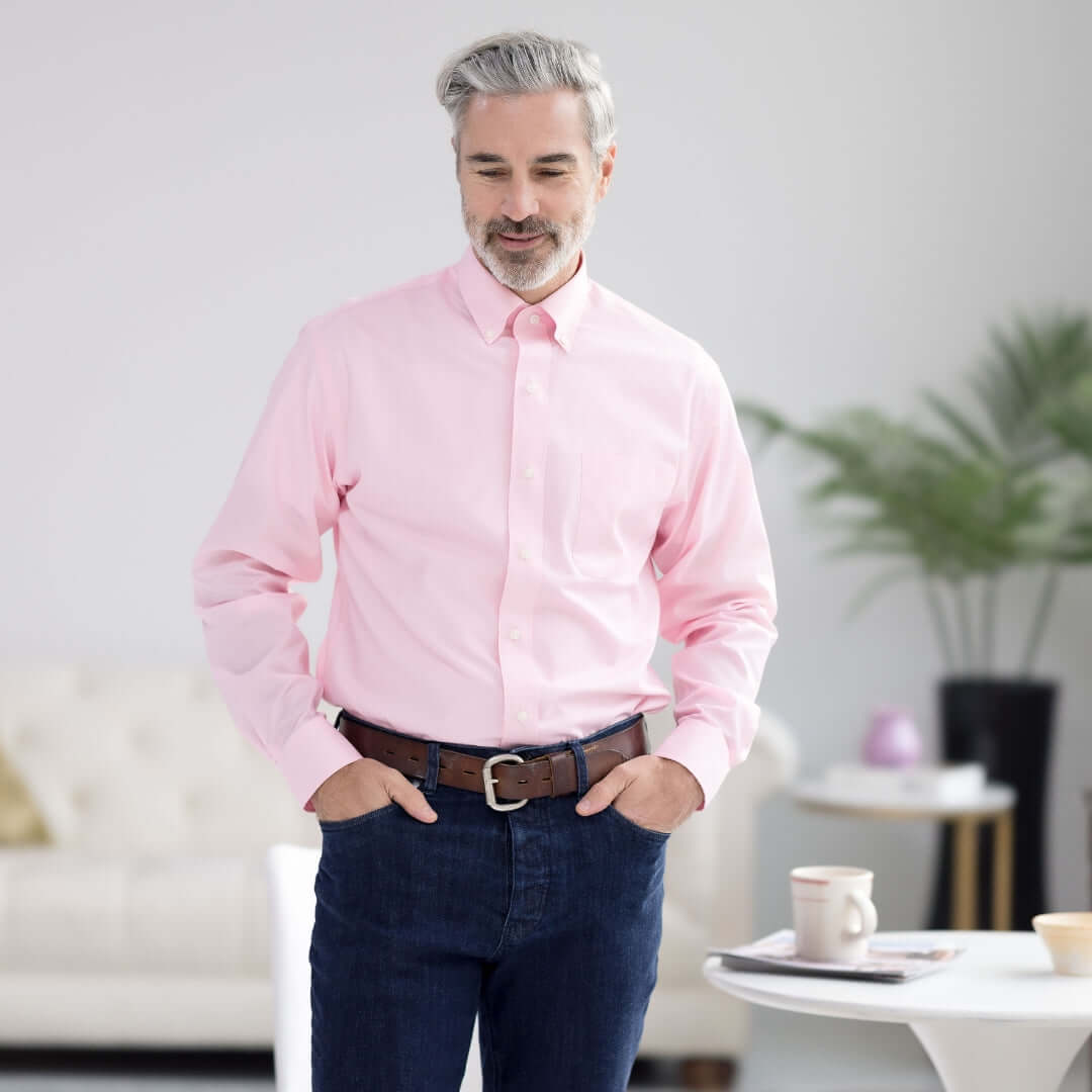Man wearing a pink long sleeve button-down collar shirt, featuring magnetic closures, in a bright living room.