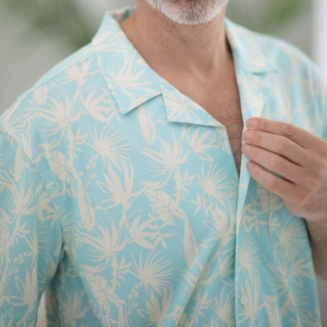 Close-up of a man adjusting a blue leaf patterned untucked short sleeve shirt, designed for comfort and mobility.